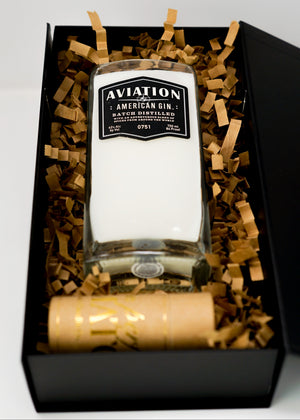 A Recycled American Gin Candle in a black gift box with brown crinkle paper, topped with a wooden cap and complemented by a natural soy candle for an elegant touch.