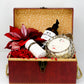 An open red gift box from Christmas Gift Baskets with body wash, a scented candle, a glittery cylinder, red leaves, and shredded paper—ideal for holiday gifting.