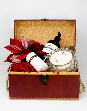 An open red gift box from Christmas Gift Baskets with body wash, a scented candle, a glittery cylinder, red leaves, and shredded paper—ideal for holiday gifting.