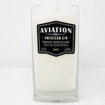 The Recycled American Gin Candle is a white natural soy candle in a rectangular glass container featuring a black label with "Aviation American Gin, Batch Distilled, 42% Alc By Vol, 750 ml, 84 Proof." Stylish and eco-friendly.