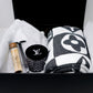 The LV Designer Gift Set includes a rolled cotton throw blanket, a black LV logo candle, a wooden tube, and a silver tool in a black box on white tissue paper—an ideal gift.