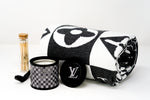 The LV Designer Gift Set features a rolled black and white cotton throw, a sleek black "LV" candle, and a glass jar of wooden matches, all arranged stylishly on a white surface.