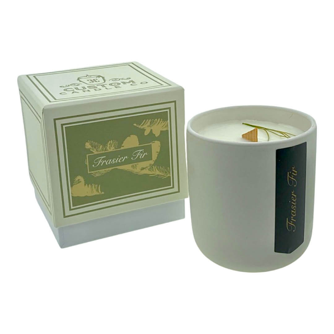 The Holiday Scented Boxed Candle – Frasier Fir Scent features a white soy wax candle in a cup labeled "Frasier Fir" beside its green and gold decorative box, perfect for a festive and delightful holiday aroma.