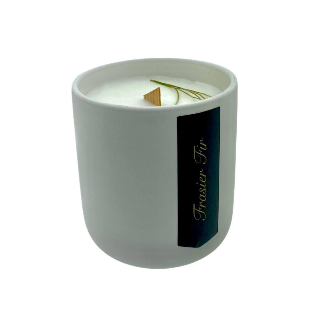 The Holiday Scented Boxed Candle – Frasier Fir Scent features white soy wax in a simple ceramic container with a wooden wick and pine sprig, making it the perfect holiday accent.
