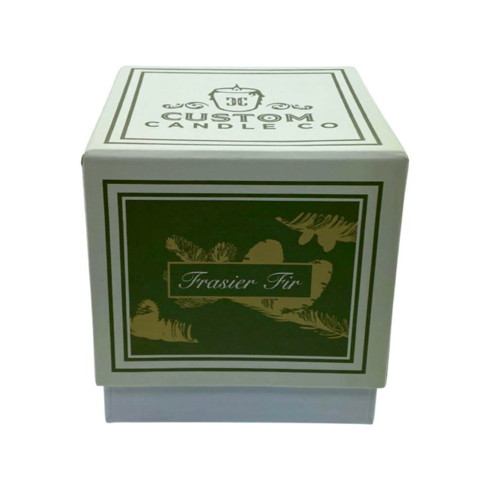 A square box labeled "Holiday Scented Boxed Candle – Frasier Fir Scent" with green and gold designs holds a festive soy wax candle.