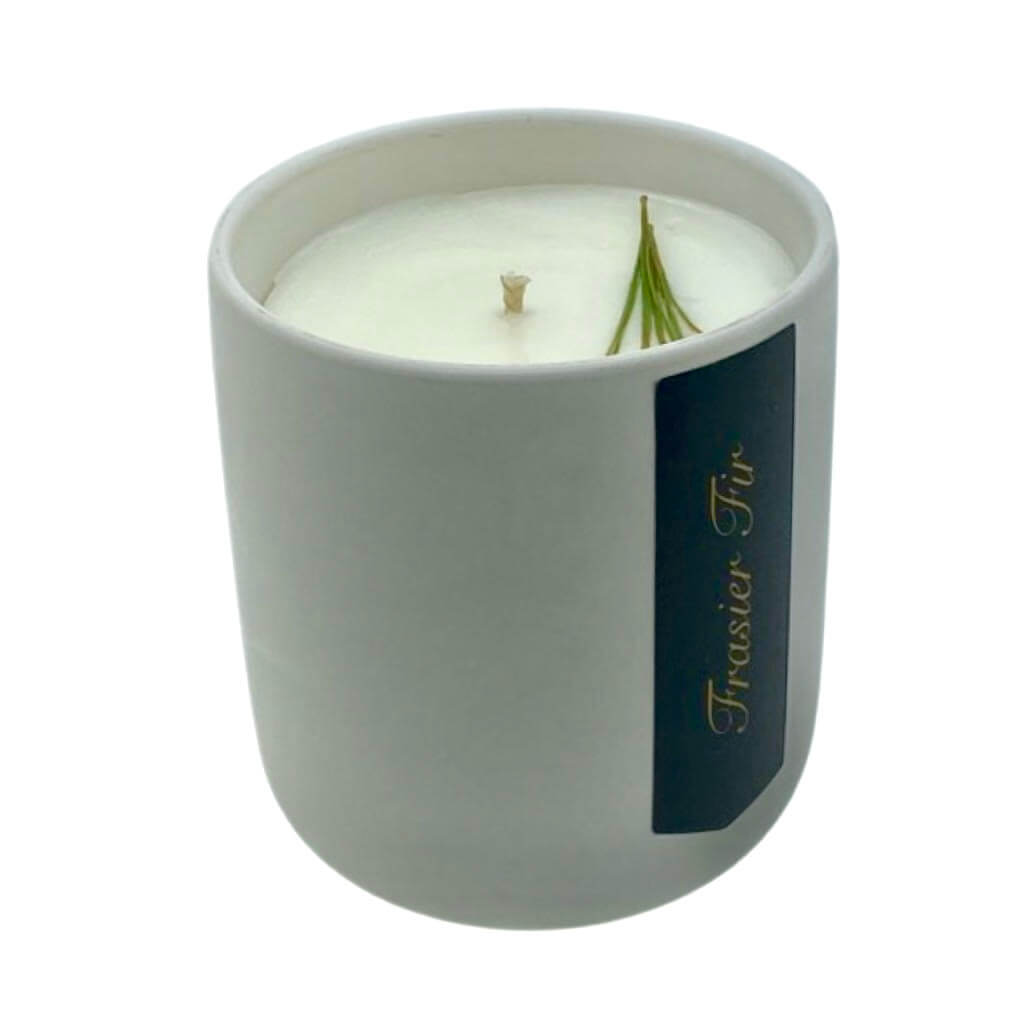 The Holiday Scented Boxed Candle – Frasier Fir Scent features white soy wax in a sleek white ceramic container with a festive pine sprig on top—an ideal candle for the holiday season.