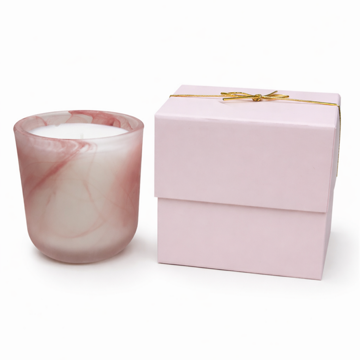 The Frosted Pink Sonoma Candle with a pink and white marbled rose scent in a glass holder sits next to a closed pink gift box tied with a thin gold ribbon.