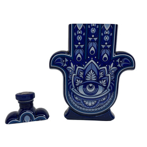 The Recycled Blanco Tequila Candle comes in a ceramic Hamsa hand bottle with a blue and white eye design and matching stopper, making it a unique holder for your favorite natural soy candle.