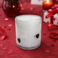 Frosted glass candle holder with heart designs on a red surface with roses, candles, and gift boxes.