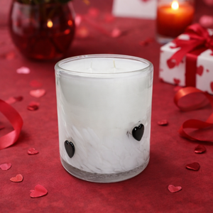 Frosted glass candle holder with heart designs on a red surface with roses, candles, and gift boxes.