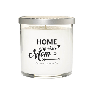 A hand-poured soy candle in a white glass jar with a silver lid. The label says: "Home is where mom is" Custom Candle Co in black decorative text.