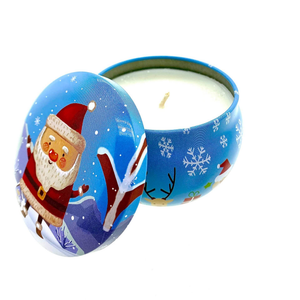 The Blue Santa Holiday Tin Candle features a festive Christmas design with Santa, snowflakes, and winter scenery on a round metal tin. Its partially open lid reveals white soy wax with a refreshing pine forest scent.