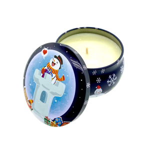 The Dark Blue Snowman Holiday Tin Candle features a festive snowman and gift design on the lid, and contains a cream-colored soy wax, single wick candle with a holiday sparkle scent. The decorative lid rests beside the candle.