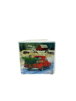 The Mini Square Christmas Candle (Red Truck Design) features a red truck with a Christmas tree on a snowy road, plus a red barn and trees—perfect for your home. Enjoy its natural soy wax and festive Holiday Sparkle scent!.