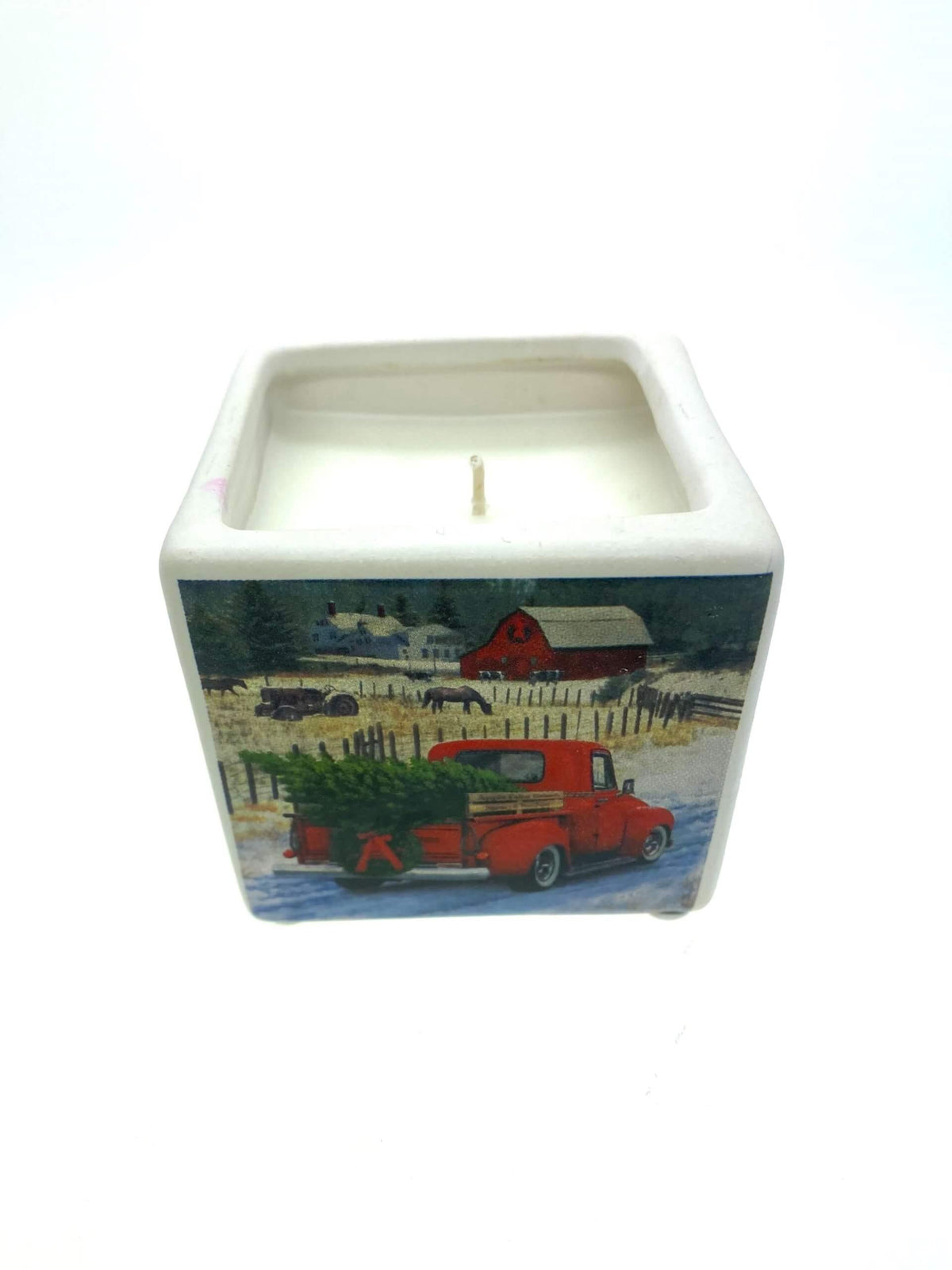 The Mini Square Christmas Candle (Red Truck Design) features a festive scene with a red truck and barn, snow-covered scenery, and holiday sparkle scent—perfect for brightening your space this season.