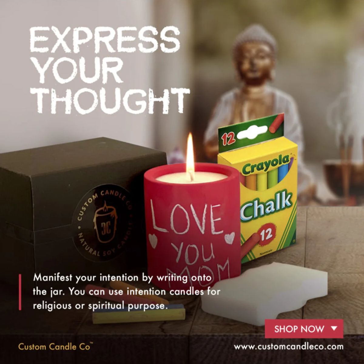 The Intention Red Candle, inscribed with "LOVE YOU," sits on the table alongside a Crayola chalk box, a black box, and a Buddha statue. Use this candle to amplify your intentions and infuse positivity into your space.