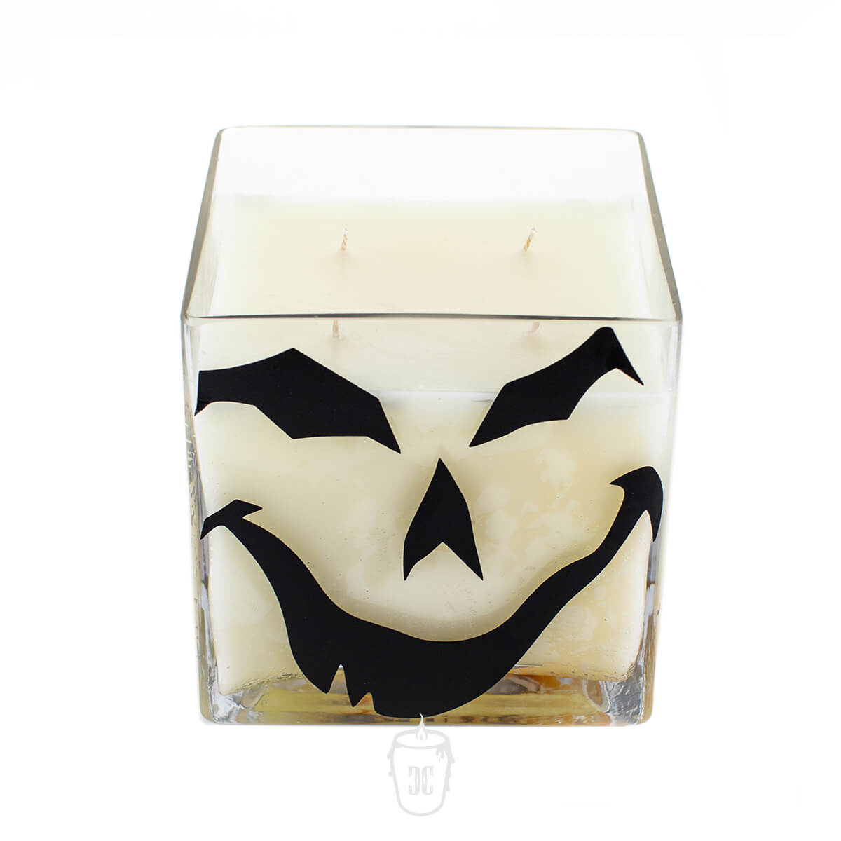 The Jack O’lantern Cube Candle 4 Wick Candle features white wax in a square glass jar with a black, smiling jack-o’-lantern face, adding a festive accent to your Halloween décor.
