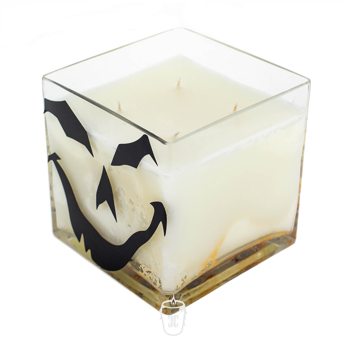 The Jack O’lantern Cube Candle 4 Wick Candle features white wax in a square glass holder with a black jack-o’-lantern face, perfect for adding festive flair to any space.