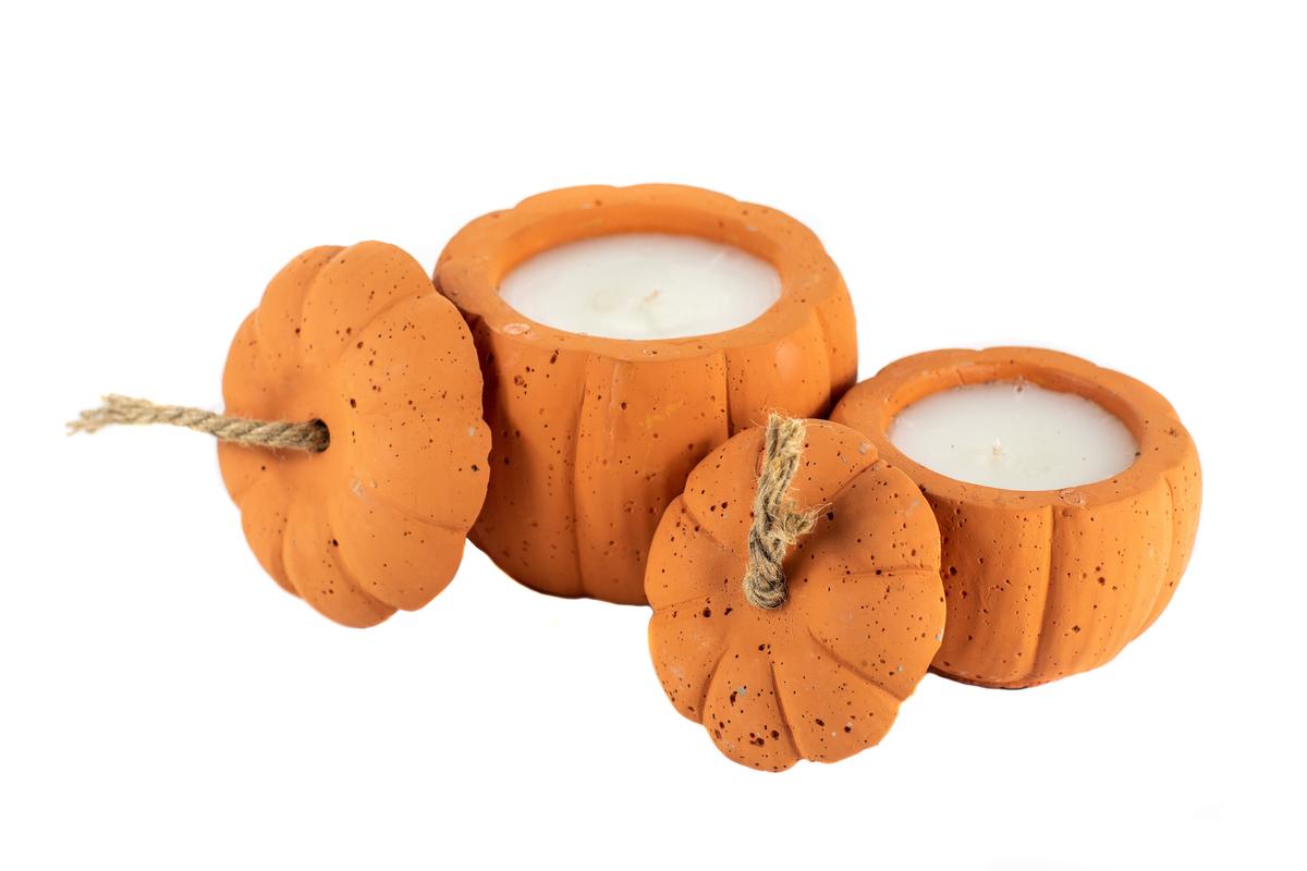 Three pumpkin-shaped candles, featuring the Orange Cement Pumpkin Candle with a rope handle, are arranged against a white background; each one displays a unique wick and charming fall-themed detail.