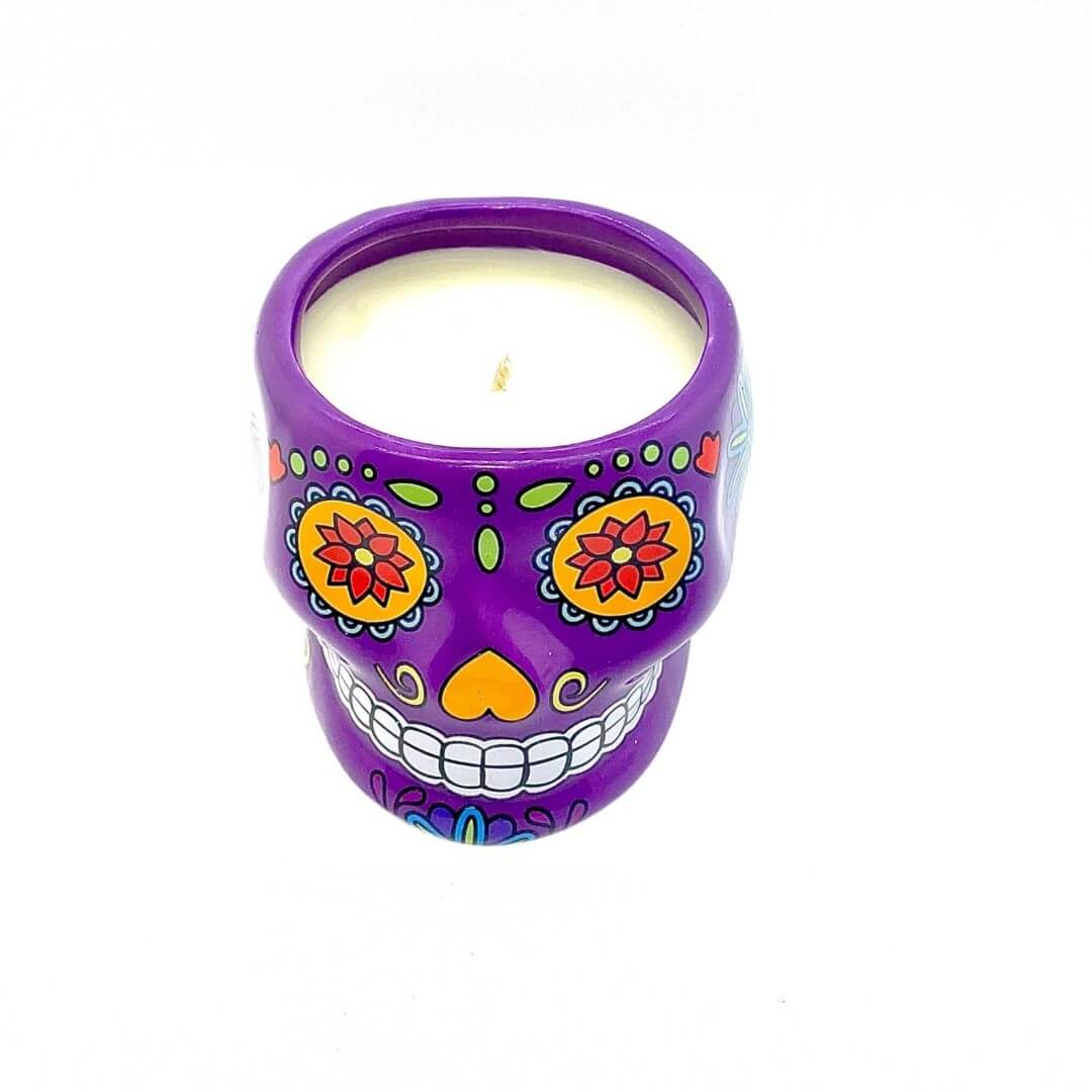 The Large Purple Ceramic Skull Candle – Nutmeg Scented features vibrant floral and geometric patterns and holds a white nutmeg-scented candle inside.