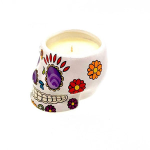 The Small White Ceramic Skull Candle – Nutmeg Scented features a white skull holder with colorful floral designs and a nutmeg-scented soy wax candle.
