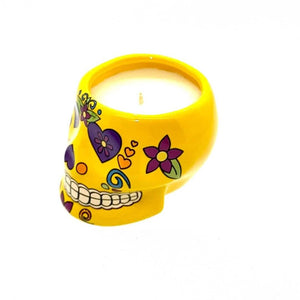 The Small Yellow Ceramic Skull Candle features colorful floral and heart designs and contains a white, nutmeg-scented soy wax candle inside.