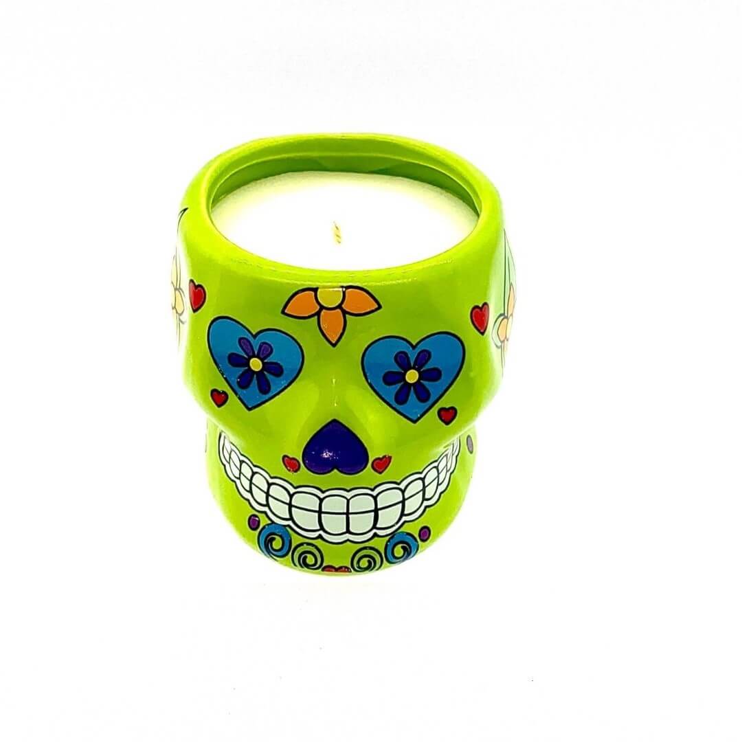 The Small Green Ceramic Skull Candle – Nutmeg Scented is a soy wax candle in a green sugar skull-shaped ceramic holder, featuring colorful floral and heart decorations.
