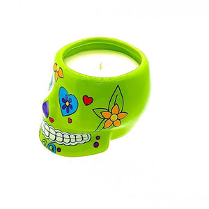 A small green ceramic skull candle holder with floral and heart designs, featuring a white, nutmeg-scented candle.