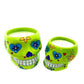 Two small green ceramic skull candle holders, nutmeg scented and featuring vibrant floral and heart motifs, are pictured against a white background.