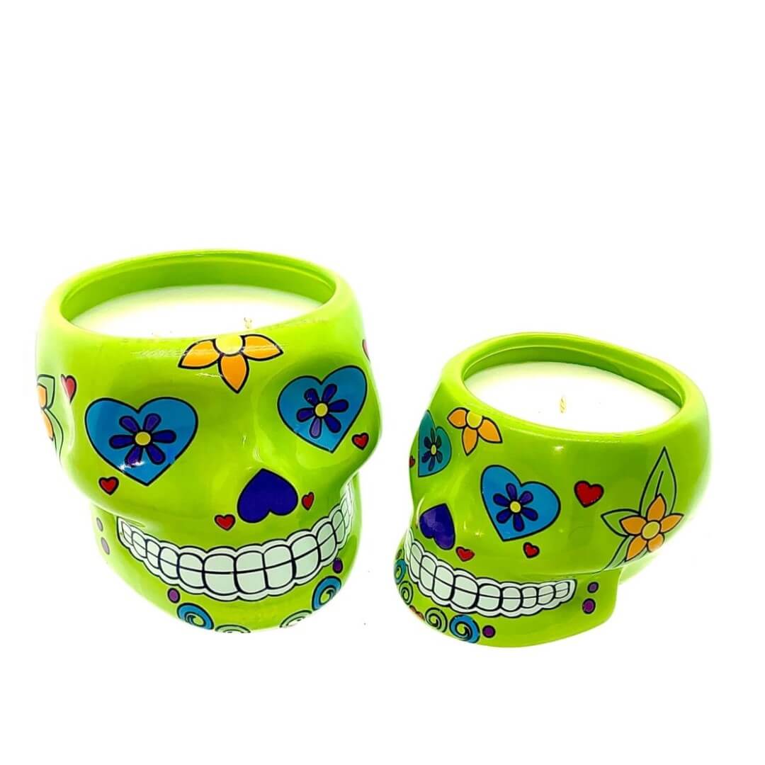 Two small green ceramic skull candle holders, nutmeg scented and featuring vibrant floral and heart motifs, are pictured against a white background.