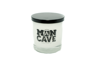 A white natural soy candle in a clear glass jar with black lid. The label reads "Man Cave"—perfect for any man cave or as a unique gift for dad.