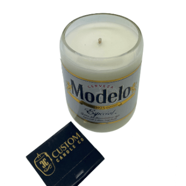 The Recycled Especial Beer Candle, hand poured in a glass made from a recycled Modelo Especial bottle, sits next to a black "3C Custom Candle Co." matchbox on a white background.