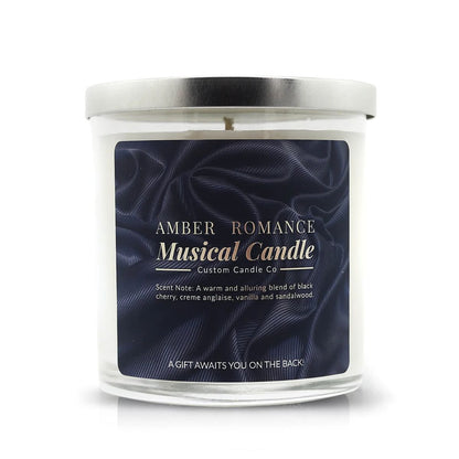 The Musical Love Candle – Amber Romance is a glass jar candle with a silver lid and dark blue label, offering black cherry, vanilla, and sandalwood scents—an ideal Valentine’s Day gift from the Musical Love Candles collection.
