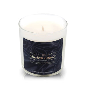 The Musical Love Candle – Amber Romance, a white scented candle in a clear glass jar with scent notes and product details, is the perfect touch for any Valentine’s Day setting against a dark background.