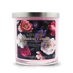 The Musical Love Candle – Love Spell is a pink scented candle in a glass jar with a silver lid, decorated with colorful flowers and labeled with fragrance and gifting details—an ideal Valentine’s Day gift.