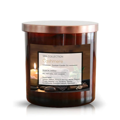 The Musical Spa Cashmere Candle, in a brown glass jar with metallic lid, offers relaxing linen, saffron, vanilla, and patchouli notes for a soothing spa experience.