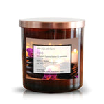 The "Musical Spa The Spa Candle" is an all-natural soy candle in a brown glass jar with a metallic lid, featuring purple orchids and spa stones—ideal for those seeking natural scented candles with relaxing fragrance notes.