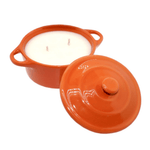 The Orange Ceramic Dutch Oven Candle – Banana Nut Bread Scent features a white soy wax candle with two wicks in an orange ceramic container, shown with its matching lid resting to the side.