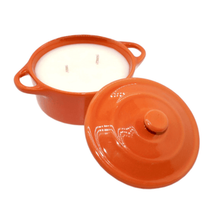 The Orange Ceramic Dutch Oven Candle – Banana Nut Bread Scent features a white soy wax candle with two wicks in an orange ceramic container, shown with its matching lid resting to the side.