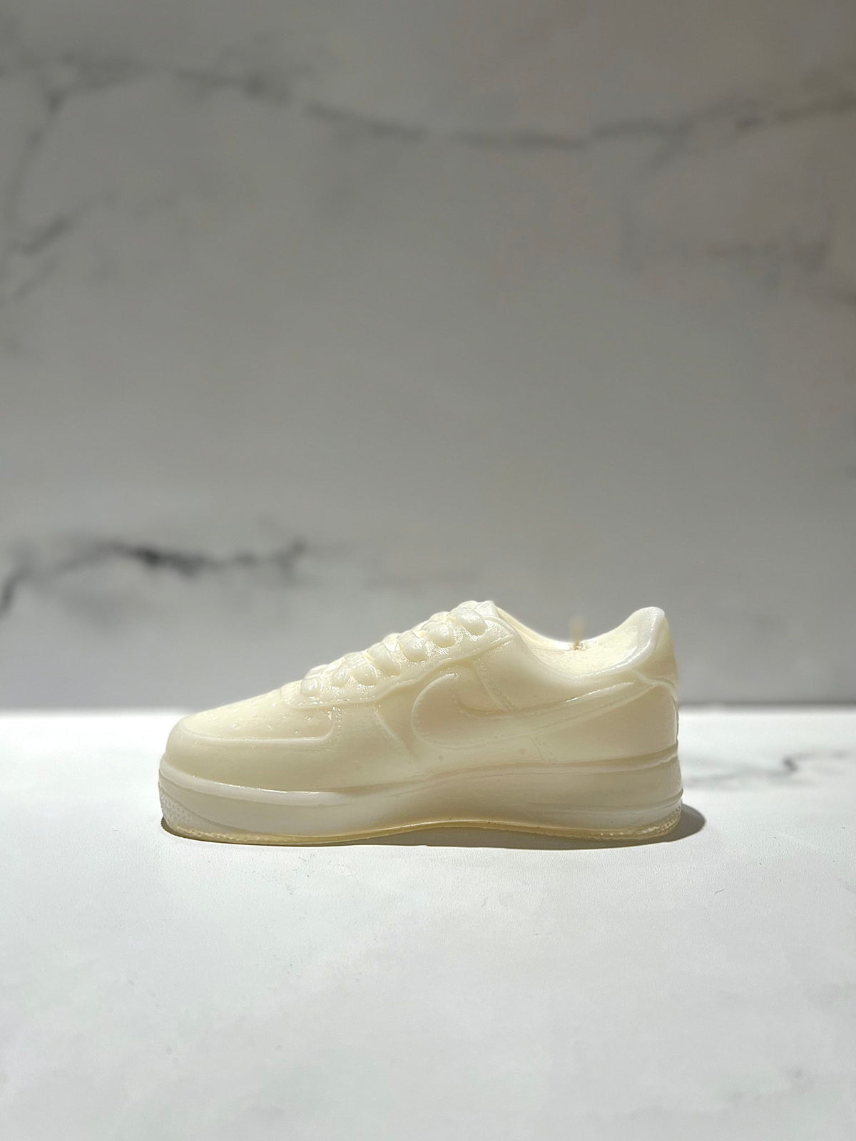 The AF1 – White Lowtop Sneaker Candle – Large (On Backorder) is a white sneaker-shaped candle inspired by athletic shoes, displayed on light marble and featuring the refreshing scent of Black Ice fragrance.