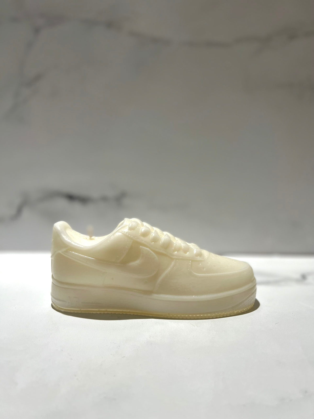 The AF1 – White Lowtop Sneaker Candle – Large (On Backorder) is designed to look like a real sneaker and is displayed on a marble surface with a plain background.