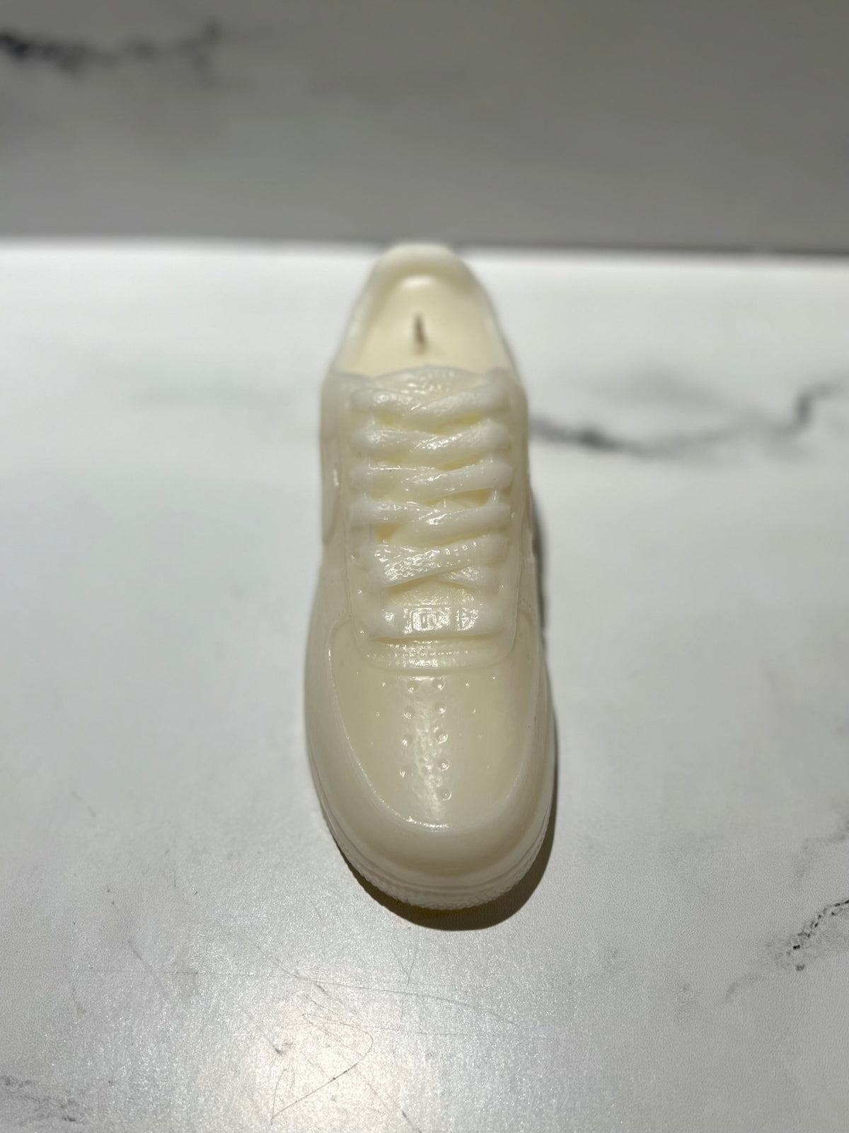 The AF1 – White Lowtop Sneaker Candle – Large (On Backorder), crafted from glossy, translucent material and infused with Black Ice fragrance, sits elegantly on a white marble surface.
