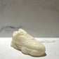 The Y500 – White Sneaker Candle – Large (On Backorder), hand poured with Black Ice fragrance, rests on a white surface with a blurred white and gray background.