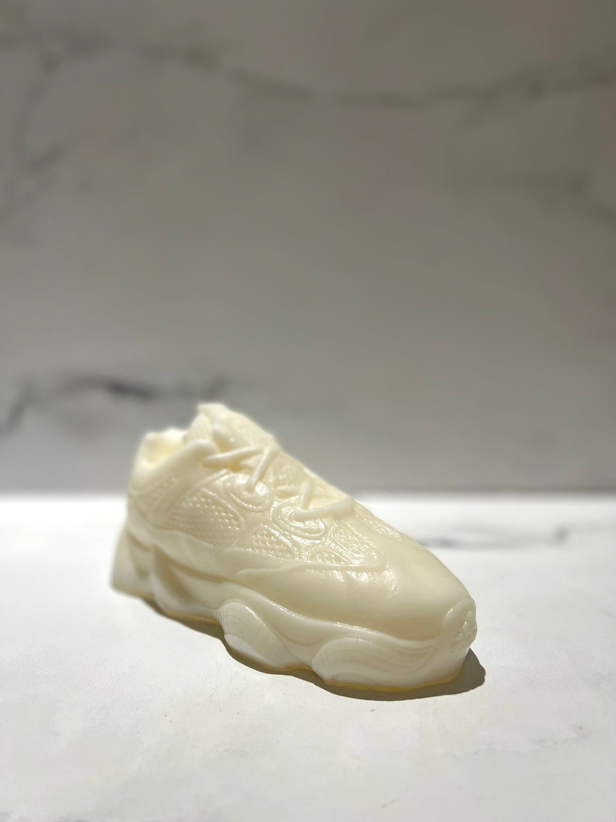 The Y500 – White Sneaker Candle – Small (On Backorder) is a hand-poured, classic shoe-shaped white candle placed on a smooth light surface with a marble background, and it may feature the refreshing Black Ice fragrance.