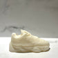 The Y500 – White Sneaker Candle – Small (On Backorder) sits on a white surface with a blurred light background, hand poured in an off-white shade and infused with Black Ice fragrance.