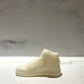 The AJ-1 White Hightop Sneaker Candle – Small (on backorder), hand poured from all natural wax, is displayed on a light surface with a blurred marble background.