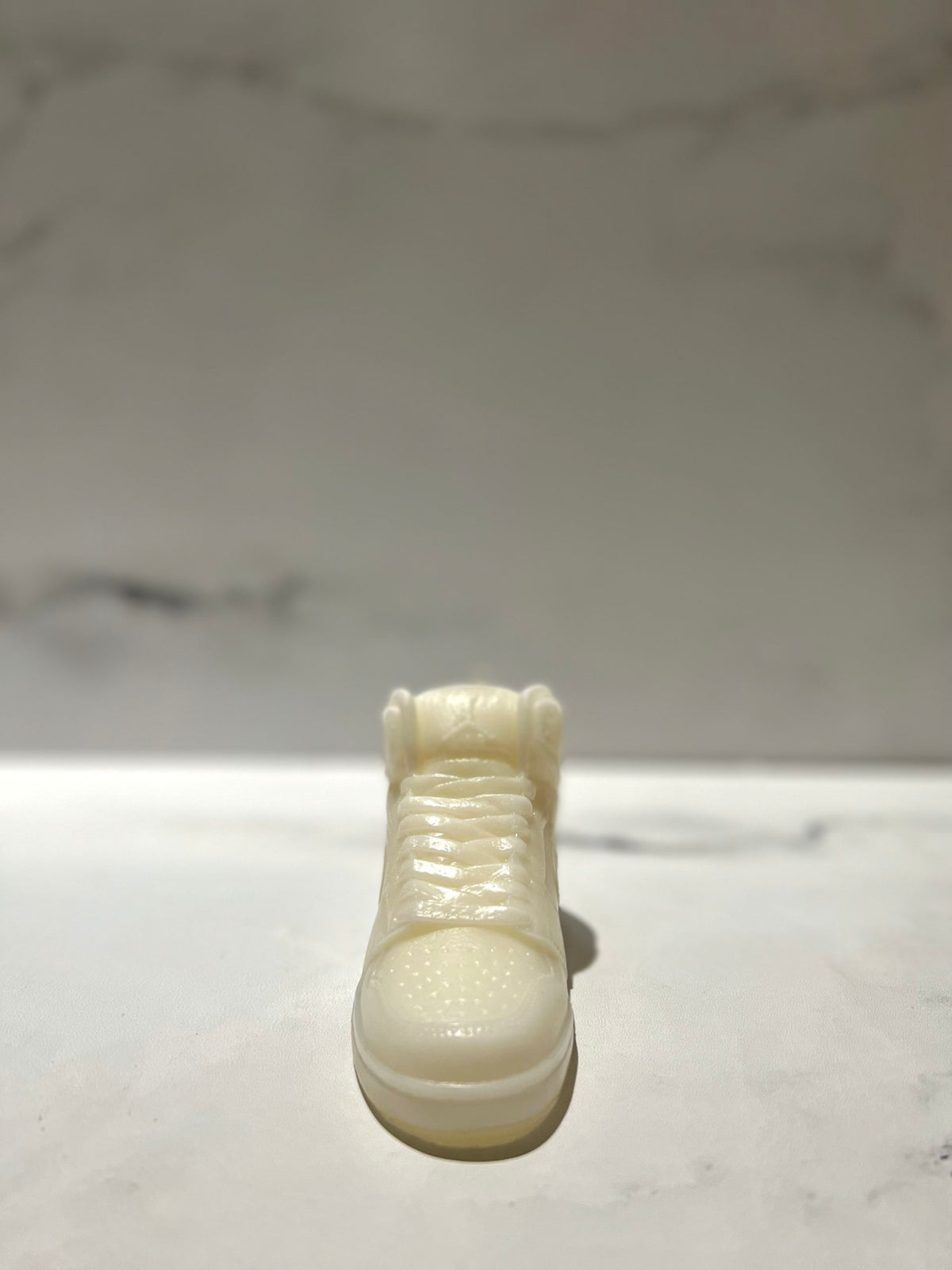 The AJ-1 White Hightop Sneaker Candle – Large (On Backorder) stands upright on a marble surface with a blurred marble background, hand poured and infused with a fresh Black Ice fragrance.