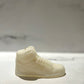 The AJ-1 White Hightop Sneaker Candle – Large (On Backorder) is hand poured and crafted to resemble a high-top sneaker, displayed on a light surface with a blurred marble background.
