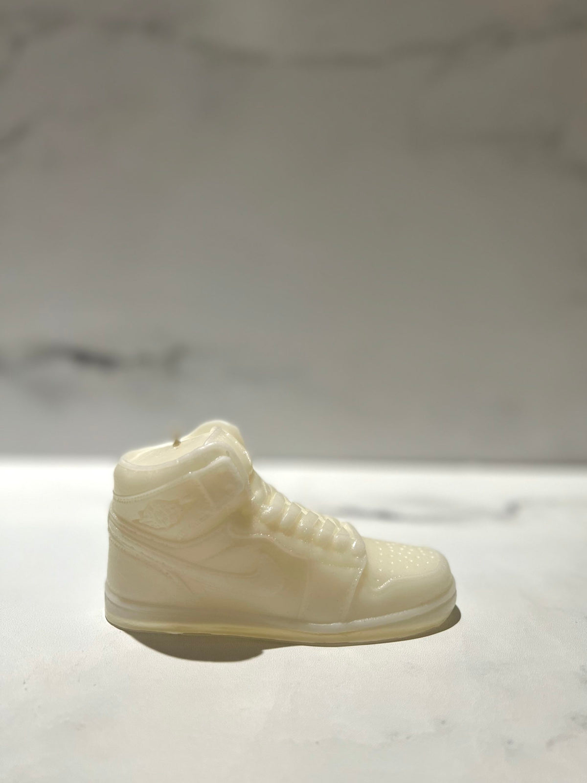 The AJ-1 White Hightop Sneaker Candle – Large (On Backorder) is hand poured and crafted to resemble a high-top sneaker, displayed on a light surface with a blurred marble background.