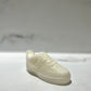 The AF1 – White Lowtop Sneaker Candle – Small (On Backorder) is a hand-poured candle shaped like a classic sneaker, featuring the fresh scent of Black Ice. It is displayed on a white surface with a blurred background.